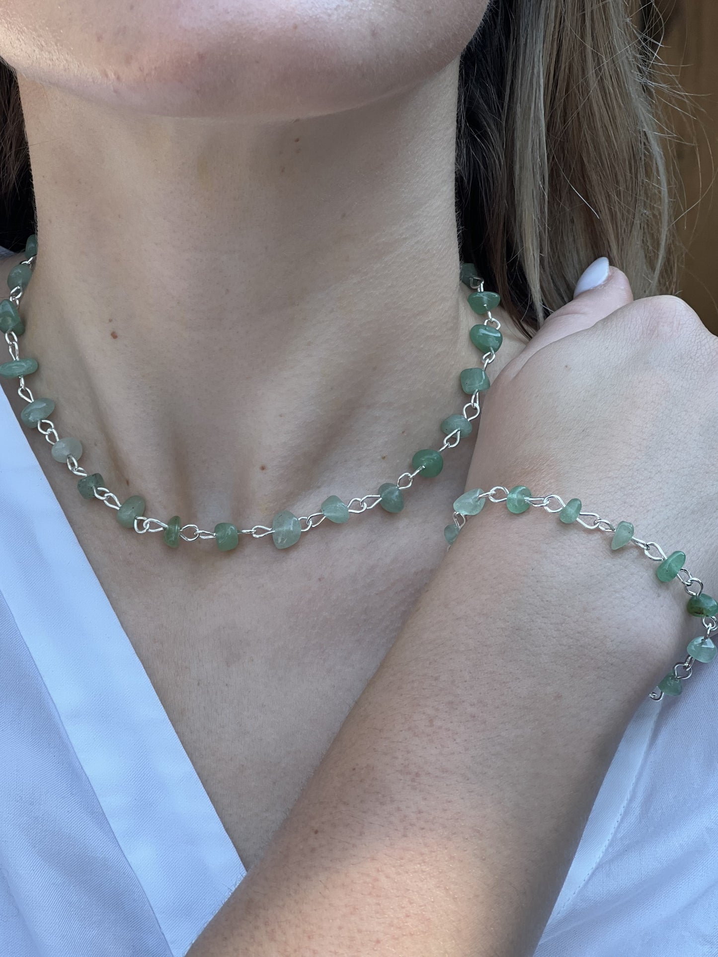 Person wearing a green beaded necklace and bracelet on a plain background
