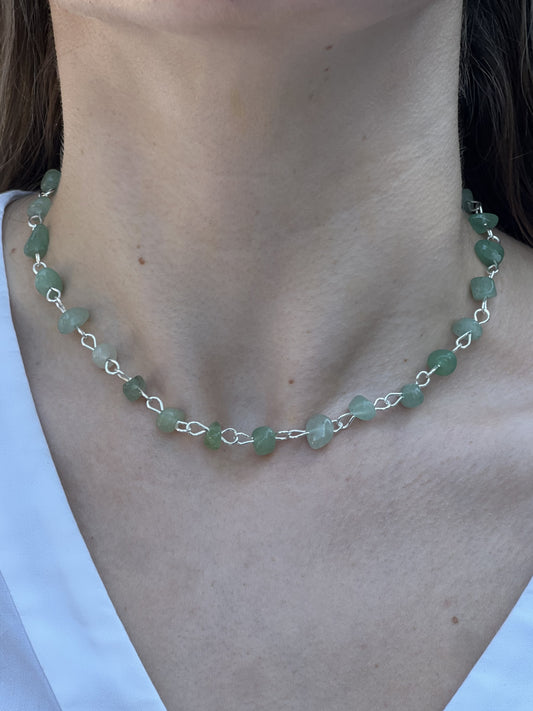 Necklace with green beads and silver chain on a person wearing a white shirt.