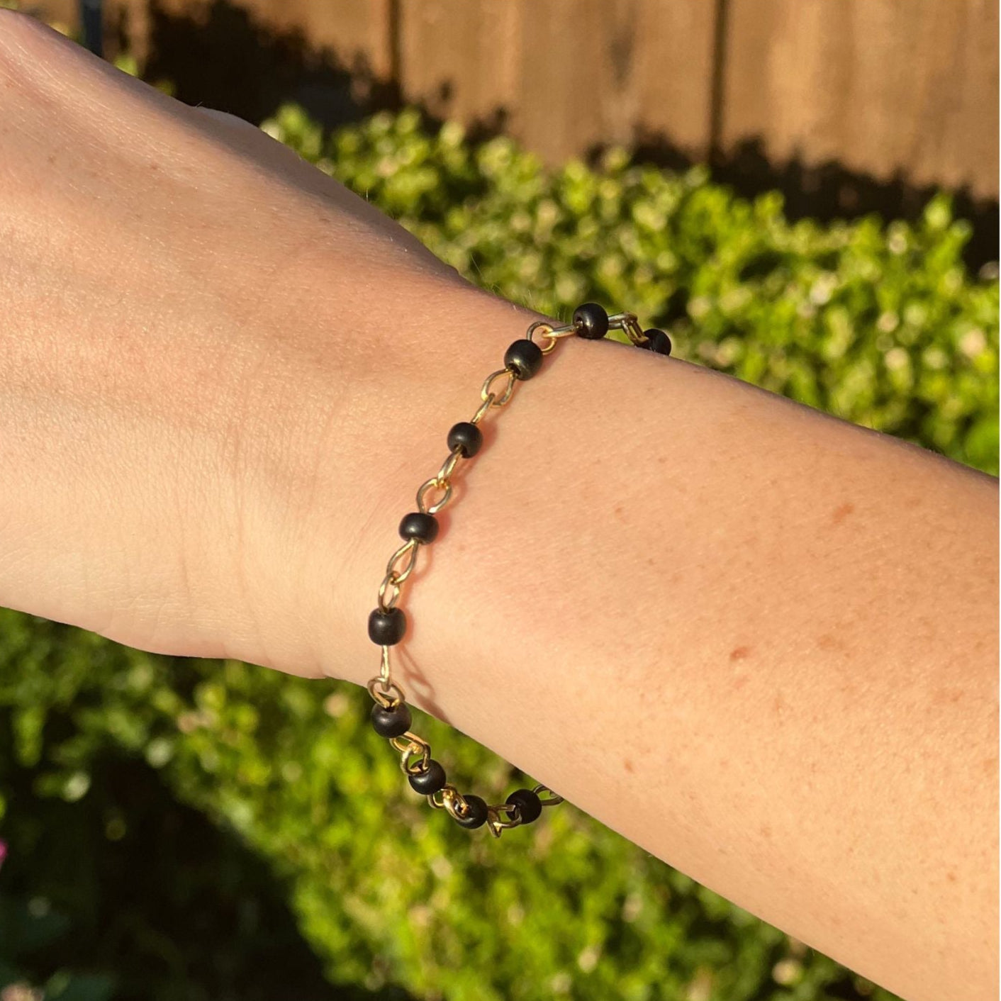 Bracelet with black beads on a wrist against a blurred green outdoor background