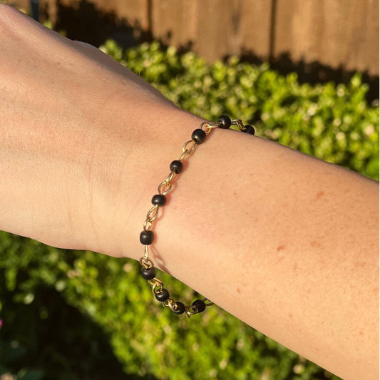 Bracelet with black beads on a wrist against a blurred green outdoor background