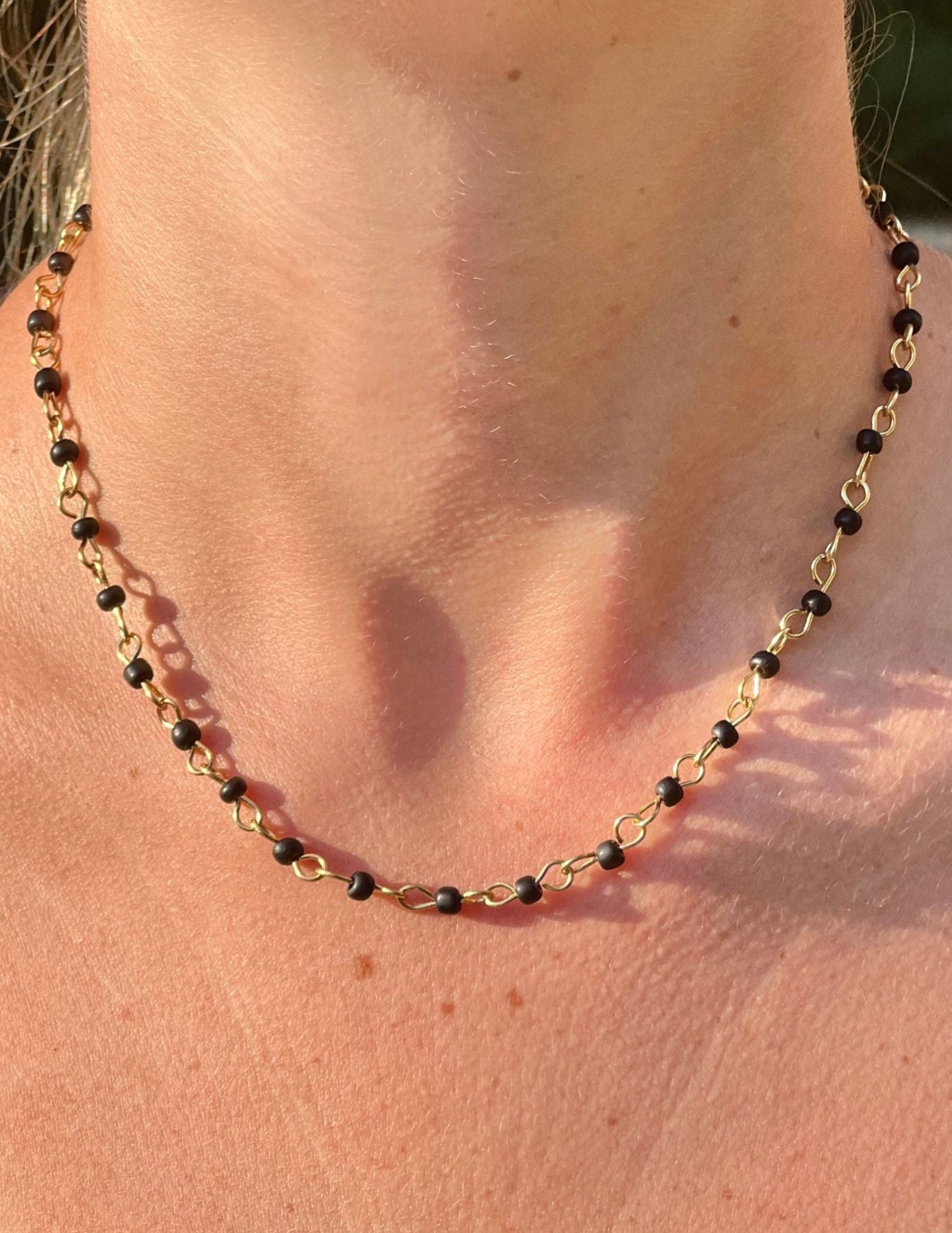 Necklace with black beads and gold chain on a person's neck
