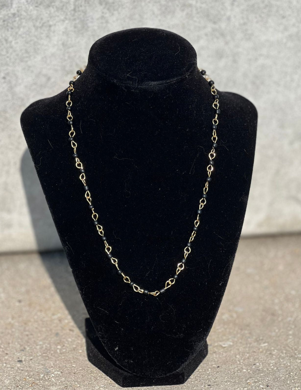 Gold chain necklace on a black velvet stand against a gray background