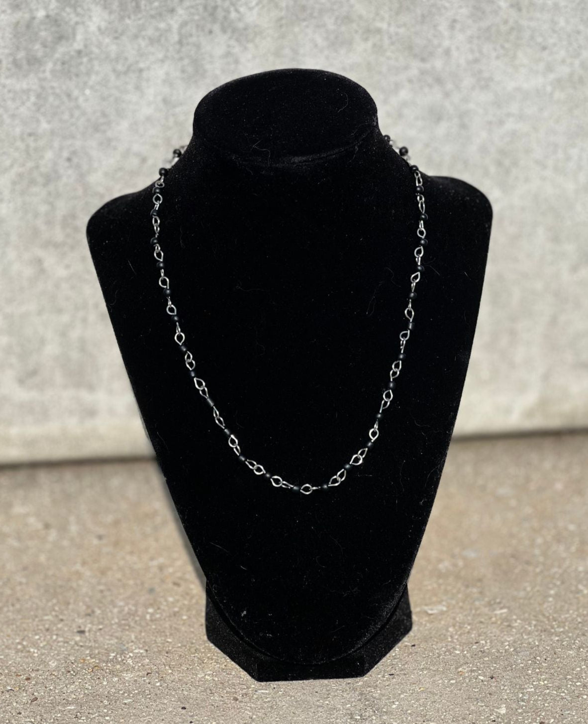 Silver chain necklace on a black velvet bust against a gray background