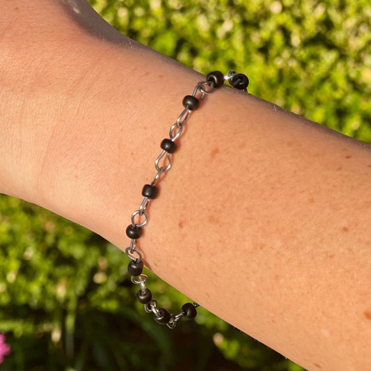Bracelet with black beads and chain on a wrist against a grassy background