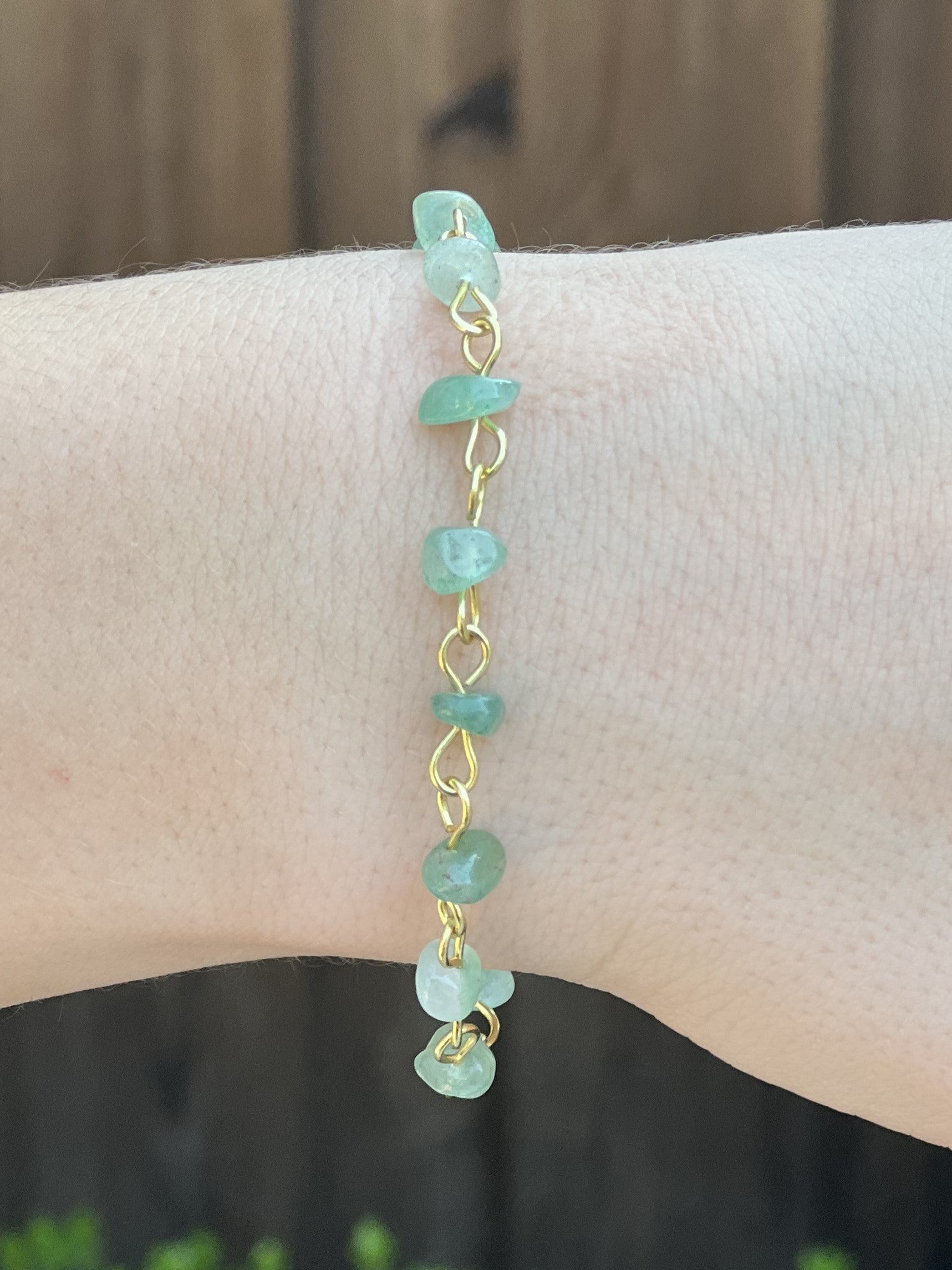 Gold bracelet with green beads on a wrist against a neutral background