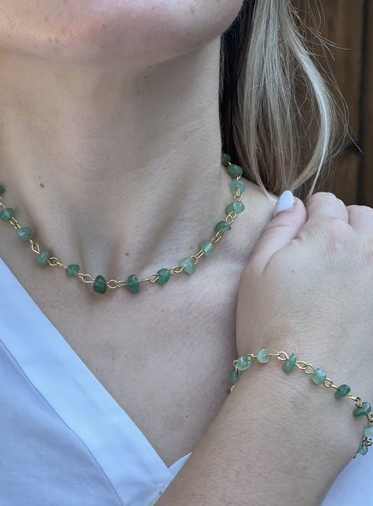 Close-up of a person wearing a gold and green beaded necklace and bracelet.