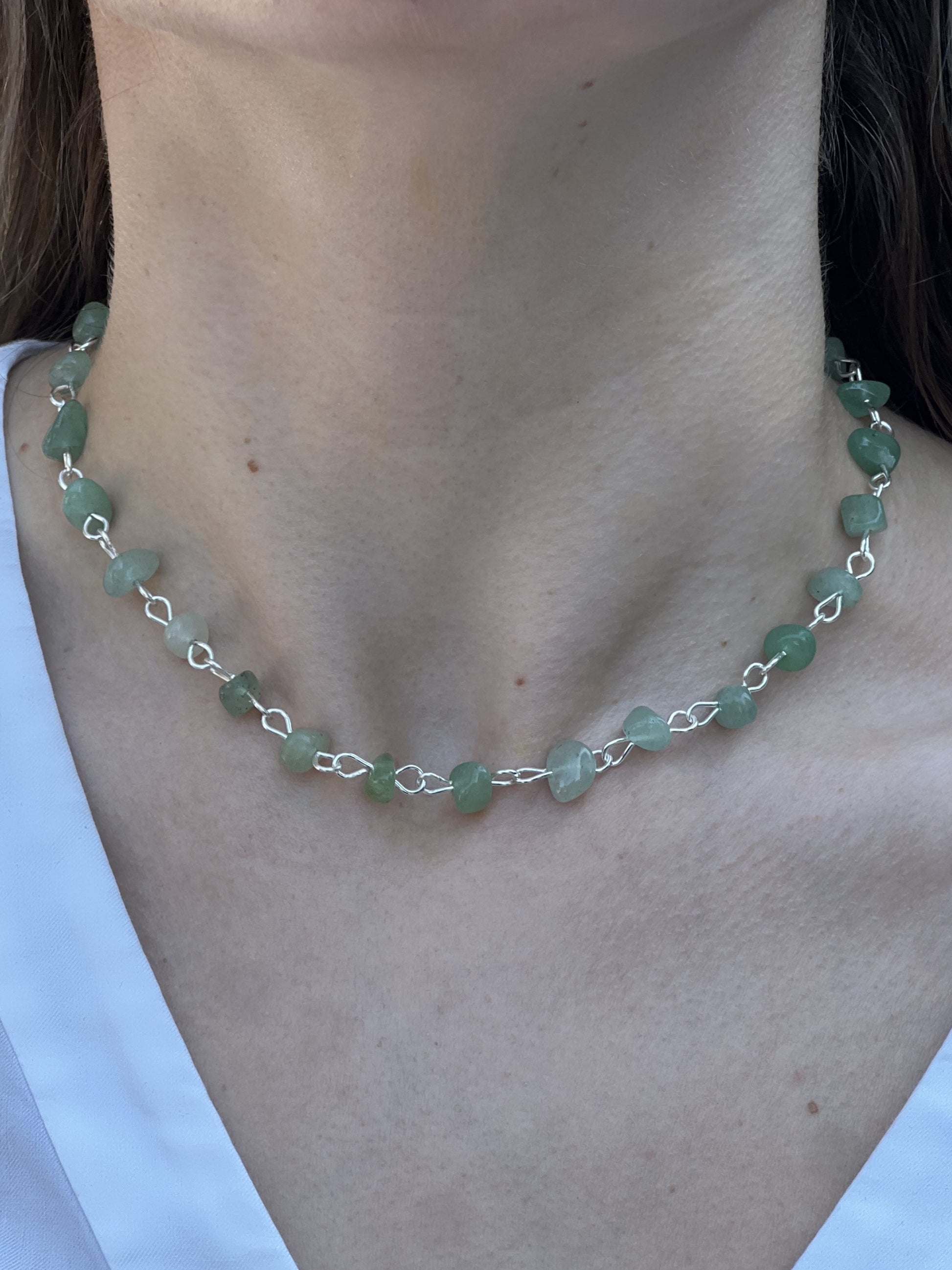 Necklace with green beads and silver chain on a person wearing a white shirt.