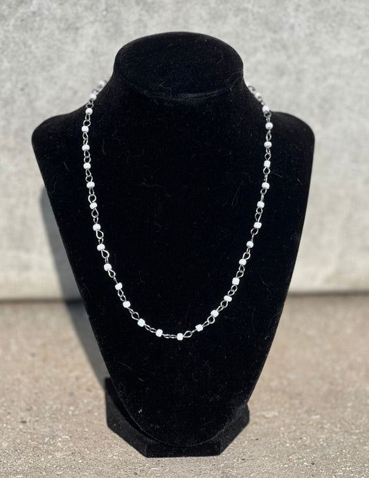 Silver necklace on a black velvet bust against a gray background